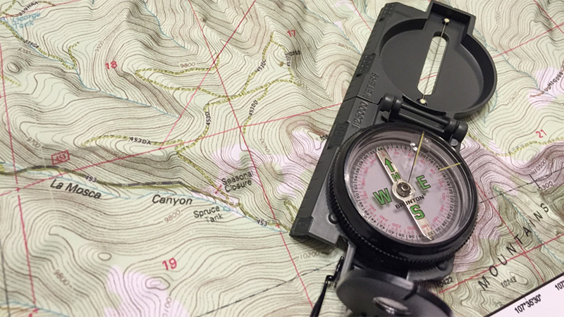 A traditional lensatic compass on a topographical map