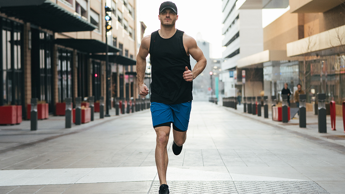 Young fit man in a black tank top running down an urban street toward the camera.