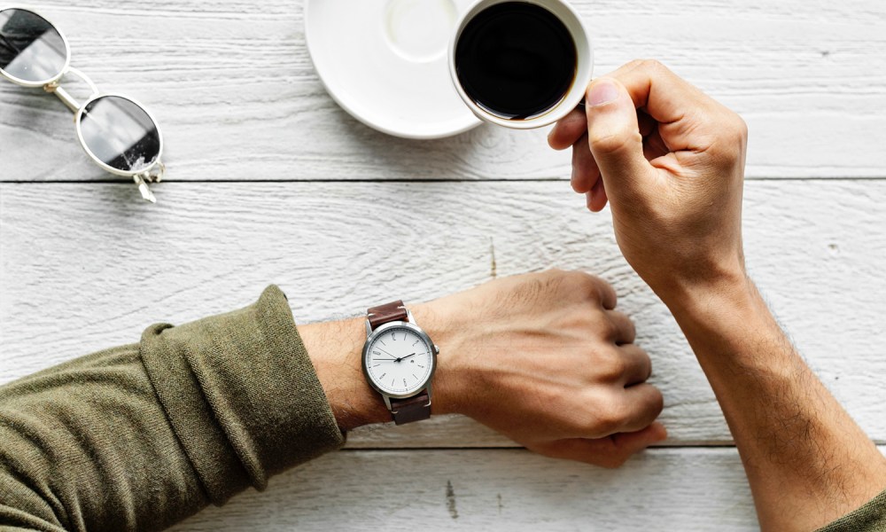 Man looking at watch and drinking coffee