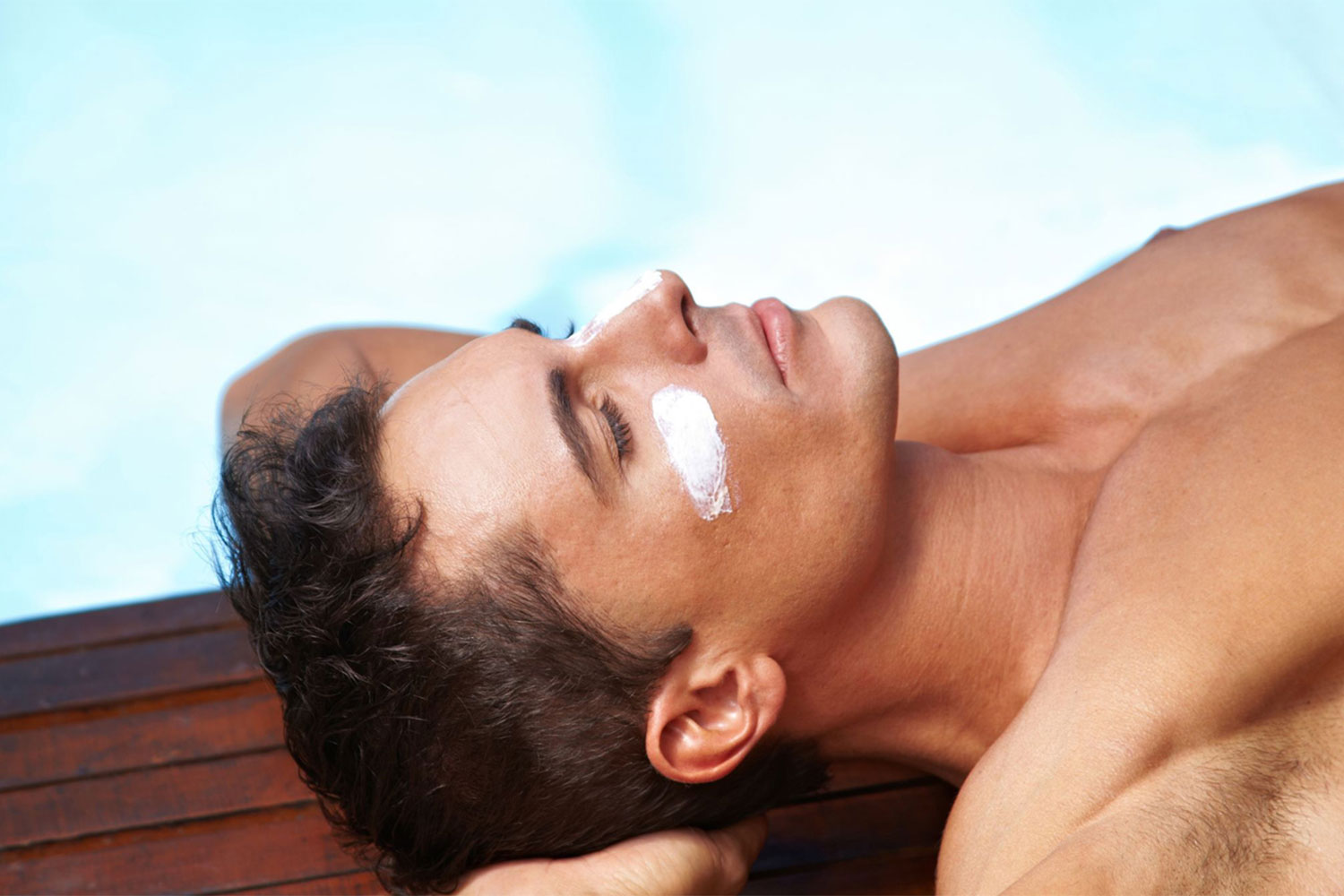 Man laying by a pool with sunscreen under his eyes