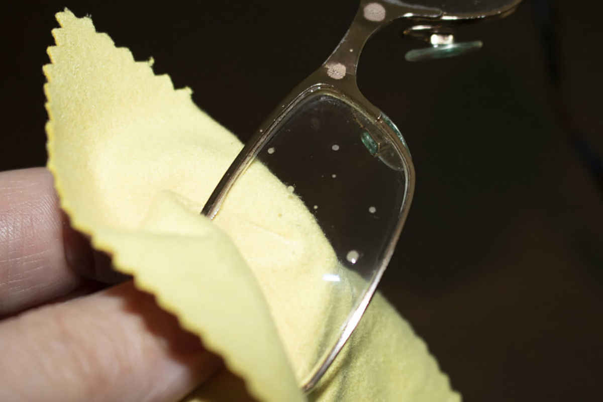 Wiping glasses lens with a yellow microfiber cloth.