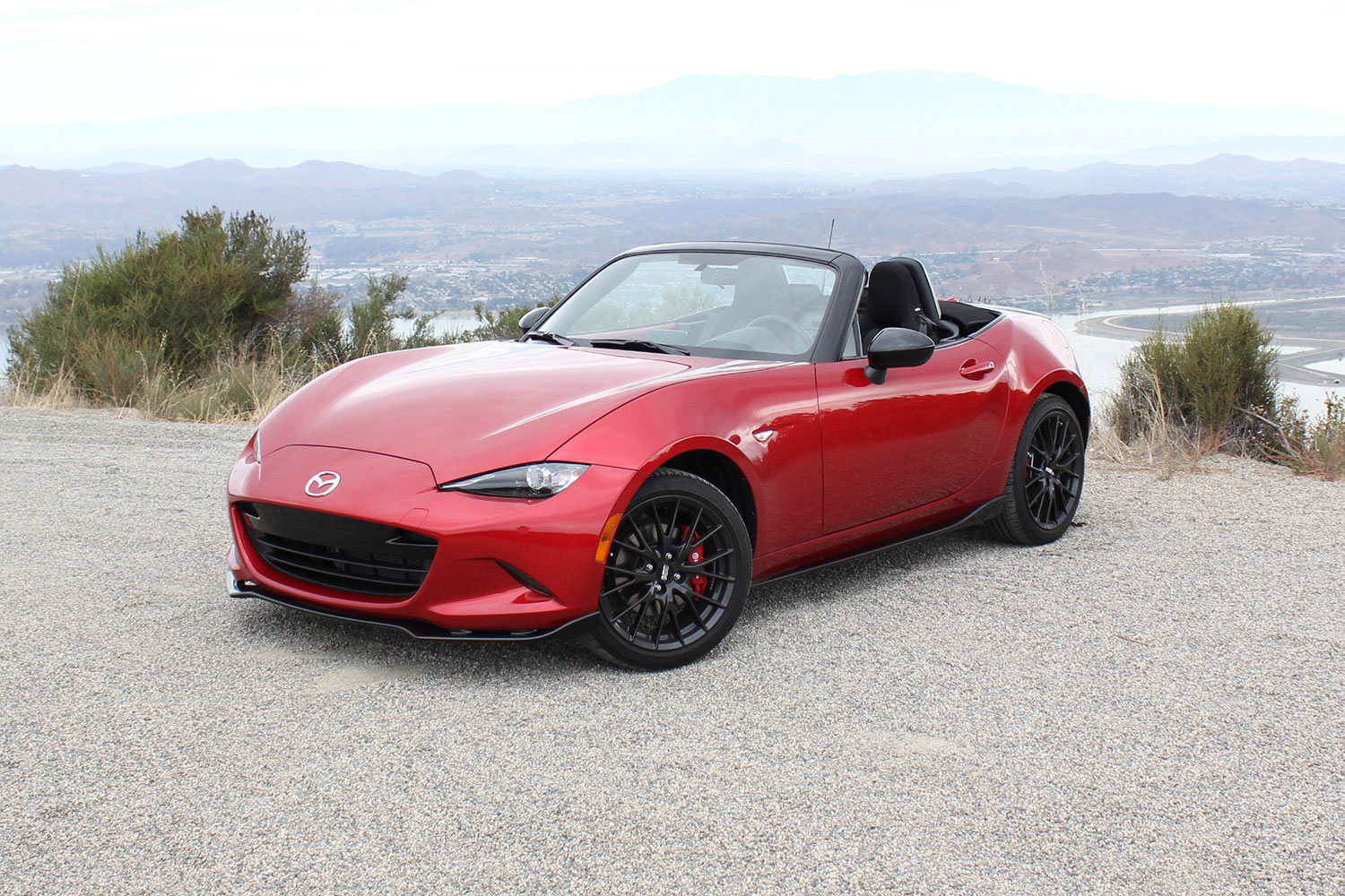 Red, open-air Mazda MX-5 Miata parked in a sandy track.