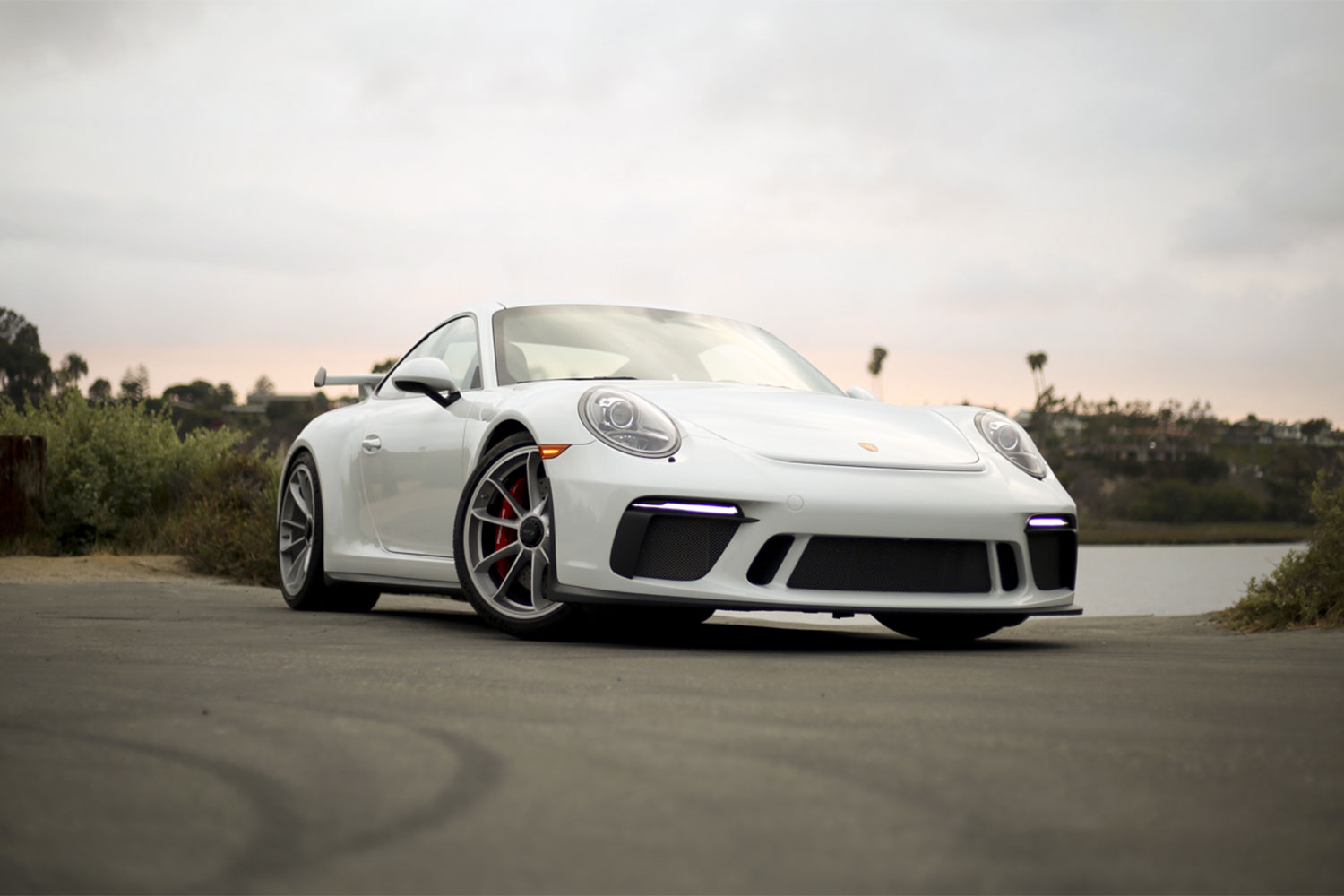 White Porsche 911 front end from the ground on asphalt in sunset.