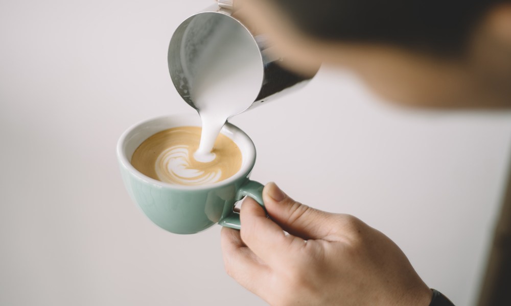 Person pouring coffee drink into a white ceramic mug