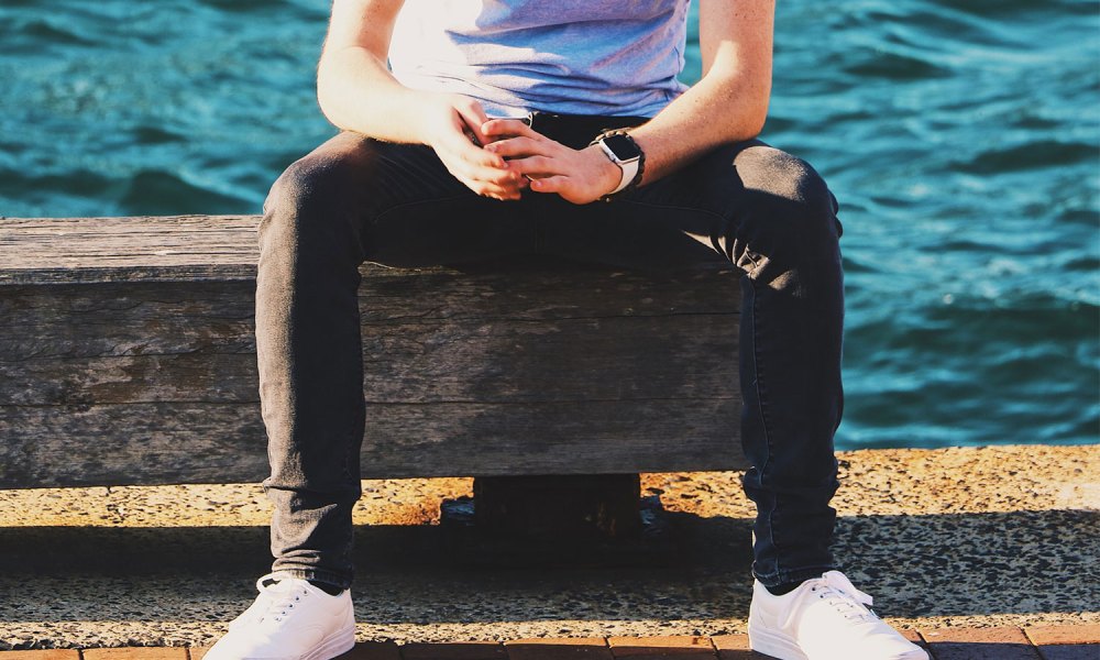 A man sitting on a concrete seat, wearing white sneakers.