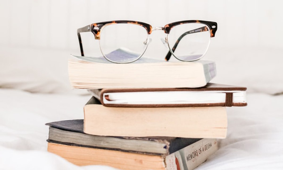 A clean pair of eyeglasses on top of books on a bedsheet.