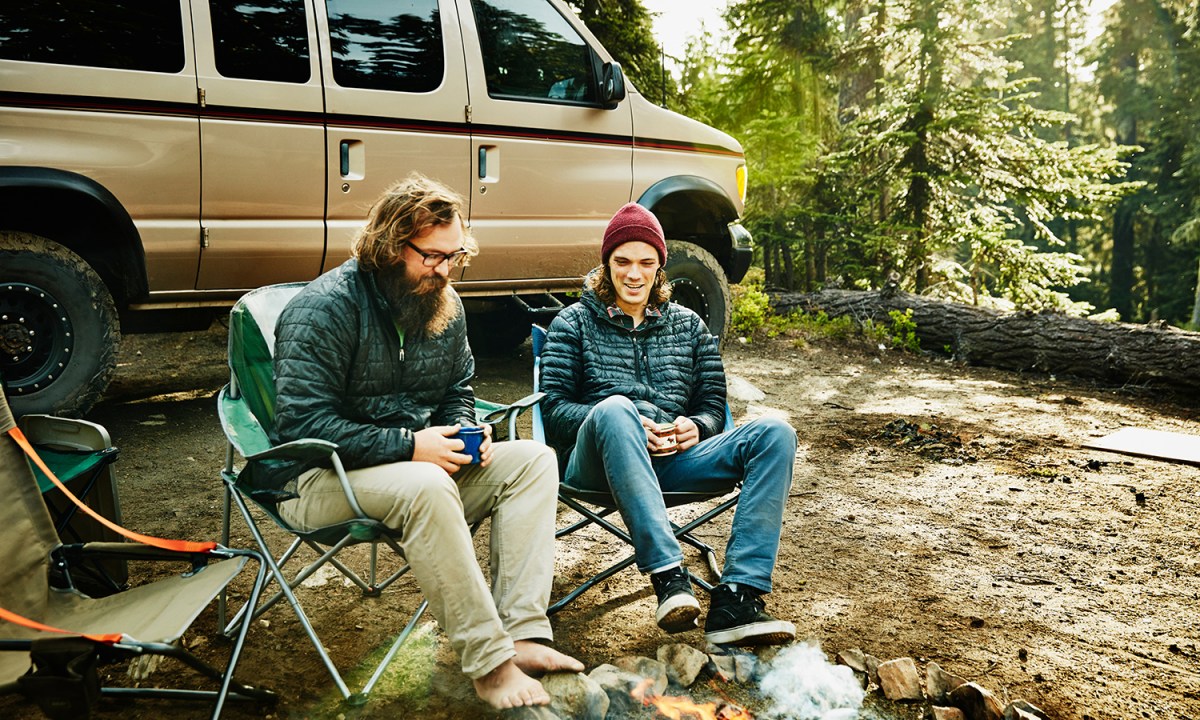 Two men in camping chars by a campfire.