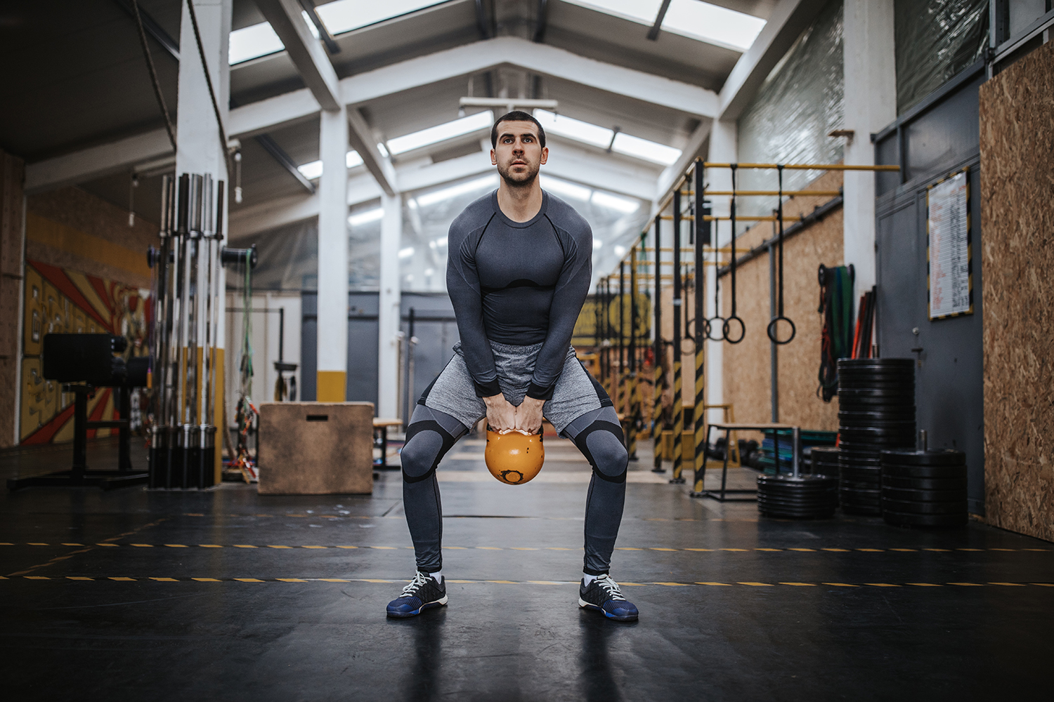 A man who's holding a kettlebell as he bends his hips and knees to perform kettlebell swings at the gym.