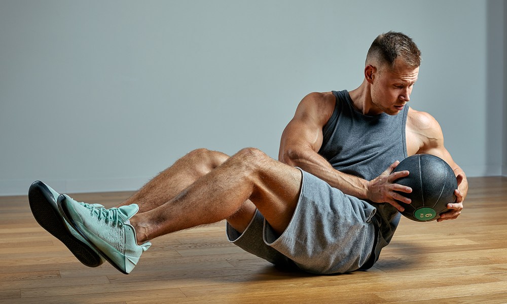 A man doing a Russian Twist while holding a medicine ball.