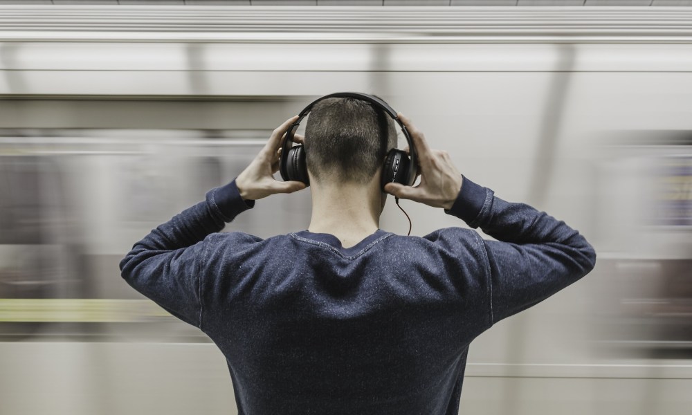 Man adjusting wireless headphones while waiting on subway platform.