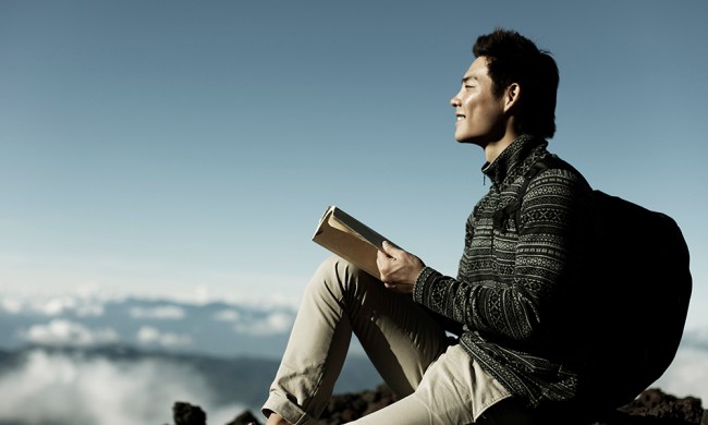 Young man reading a book in the mountains.