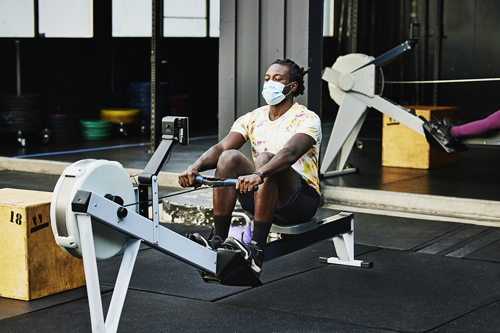 Man wearing protective face mask working out on rowing machine at outdoor gym