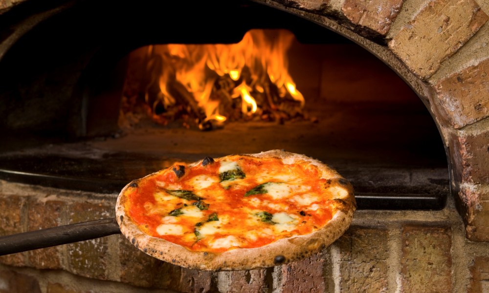 Freshly made pizza being taken out from the oven.