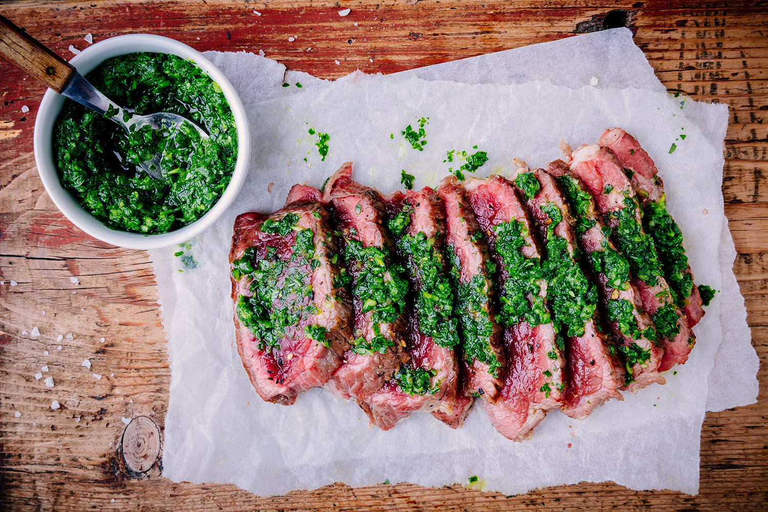 El Che Steakhouse Chimichurri presented at a wooden cutting board with extra chimichurri sauce on the side.