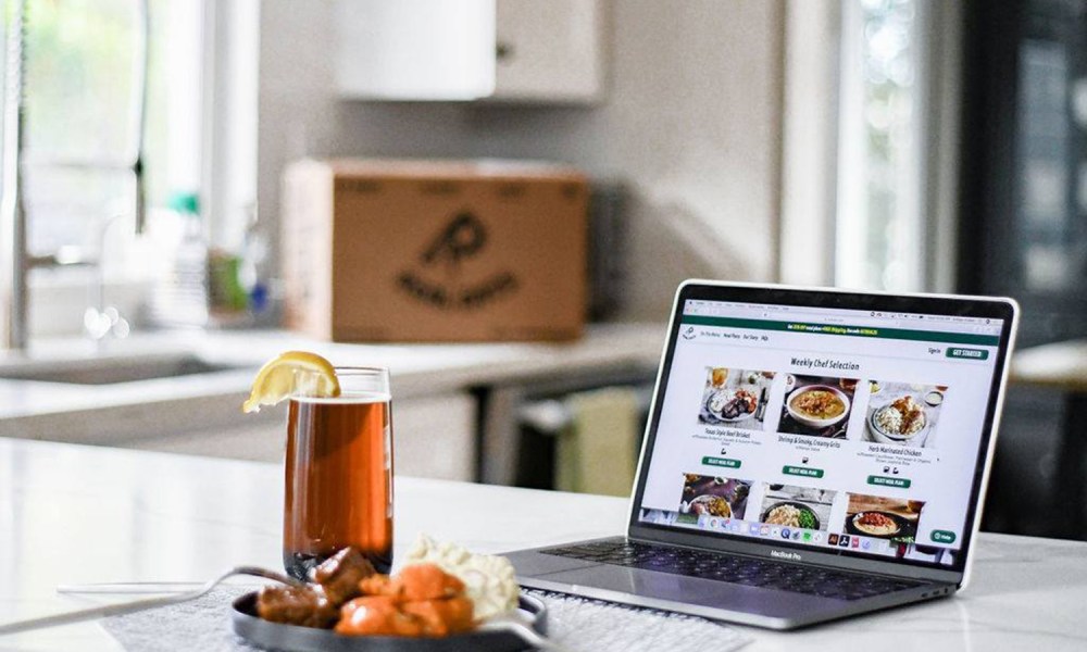 An untouched healthy dish and a drink with towel and laptop on a kitchen counter.