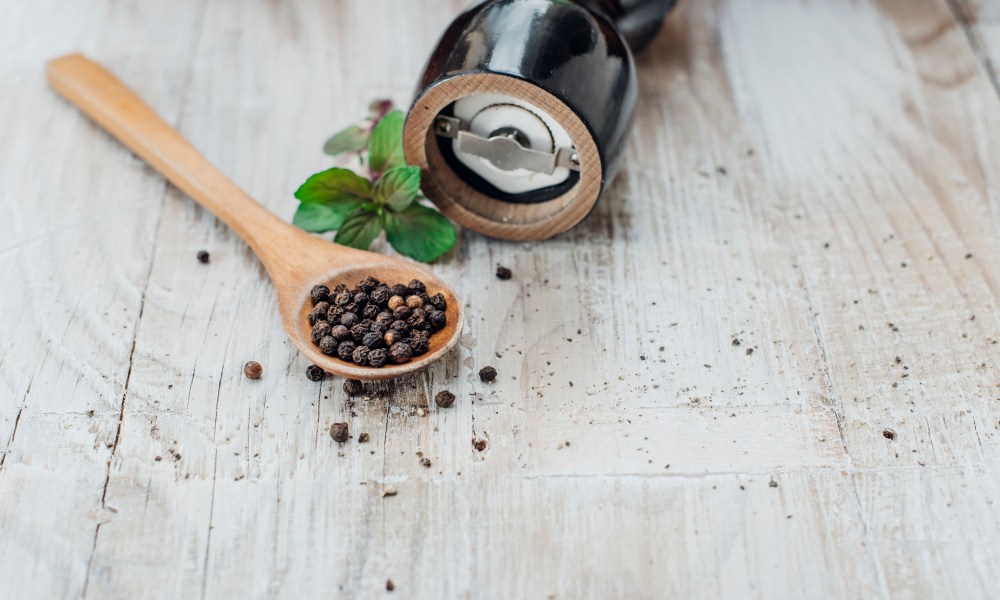 Grains of black pepper in a wooden spoon with pepper grinder