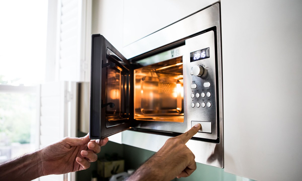 Someone lifting something out of a built-in microwave.