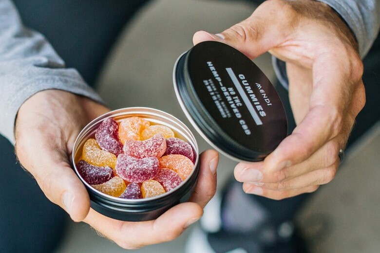 Man holding a Mendi cbd gummies in a tin.