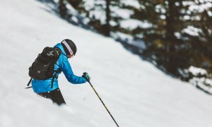 Person skiing down the slope in a blue jacket and a ski helmet