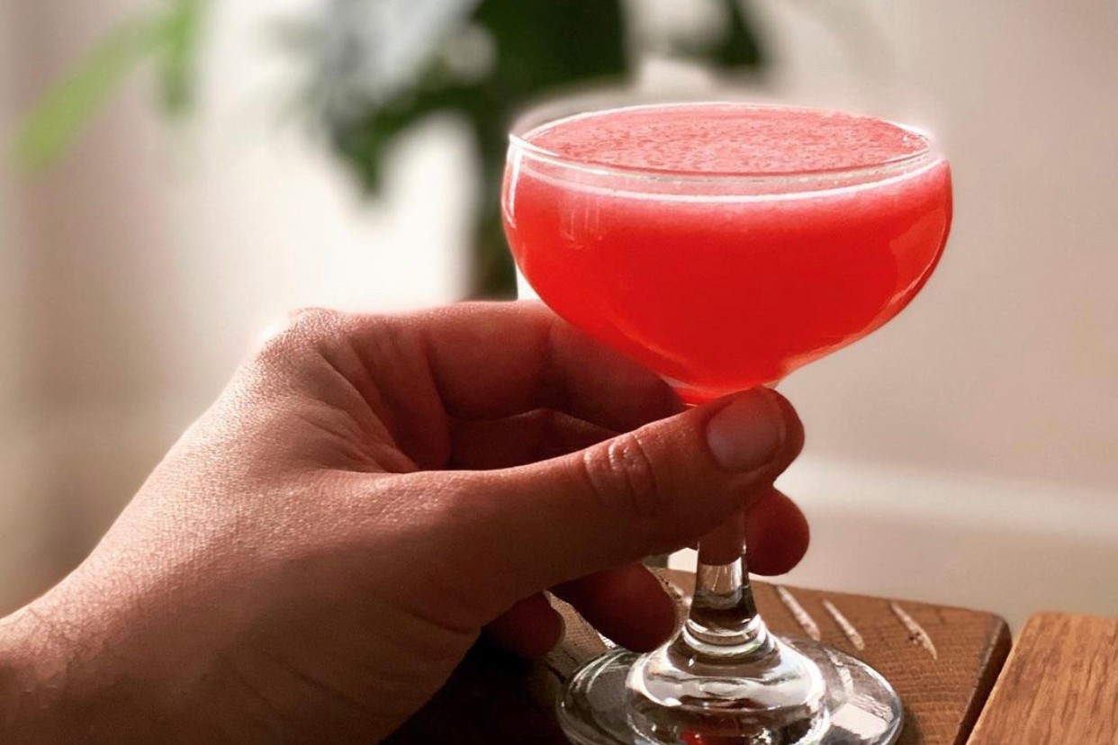 A hand holding a glass of blackberry mint daiquiri on a wooden table