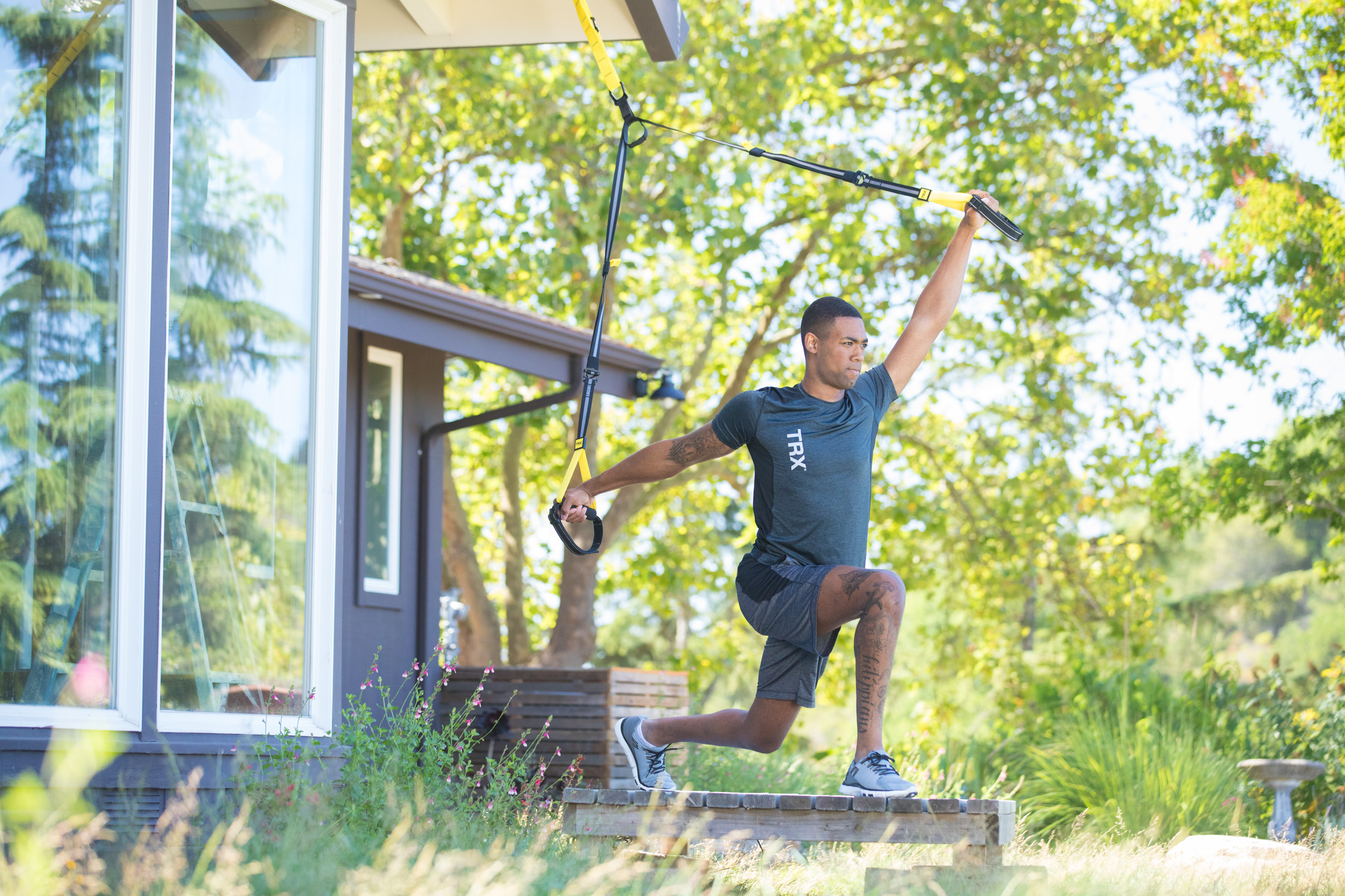 A man doing a total body workout using suspension straps outside his house with trees in the background.