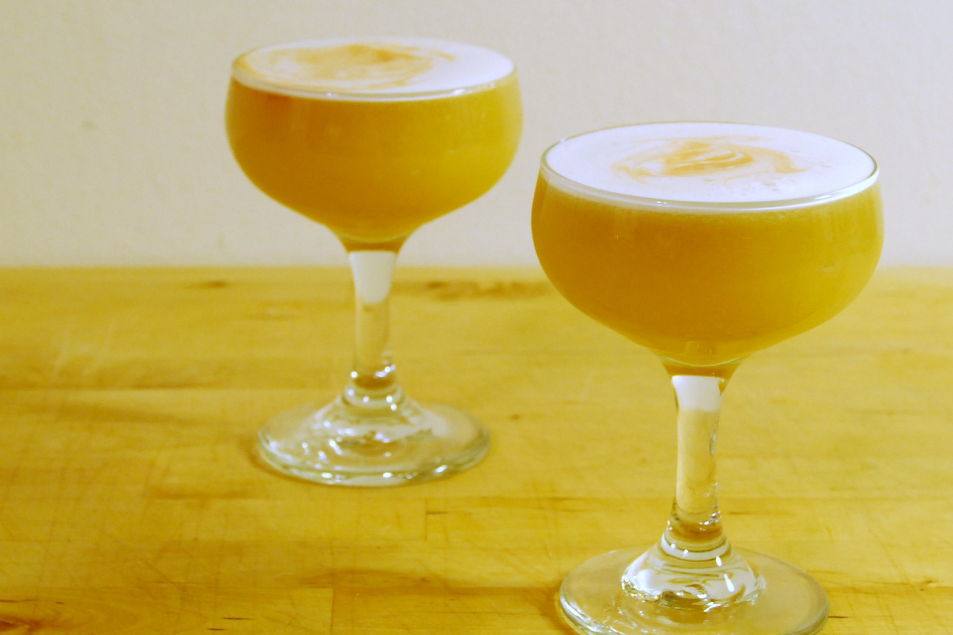 Two glasses of kumquat whiskey sour on a wooden table