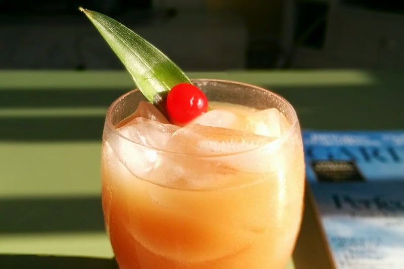 An ice-cold glass of Painkiller cocktail with cherry and leaf on a table