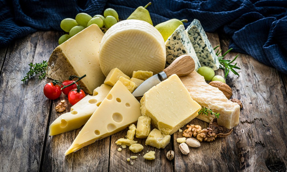 Wooden table with a delicious variety of cheeses. Cheeses included in the composition are Manchego cheese, goat cheese, emmental cheese, Roquefort cheese, Parmesan cheese and Cheddar cheese. Predominant colors are yellow and brown