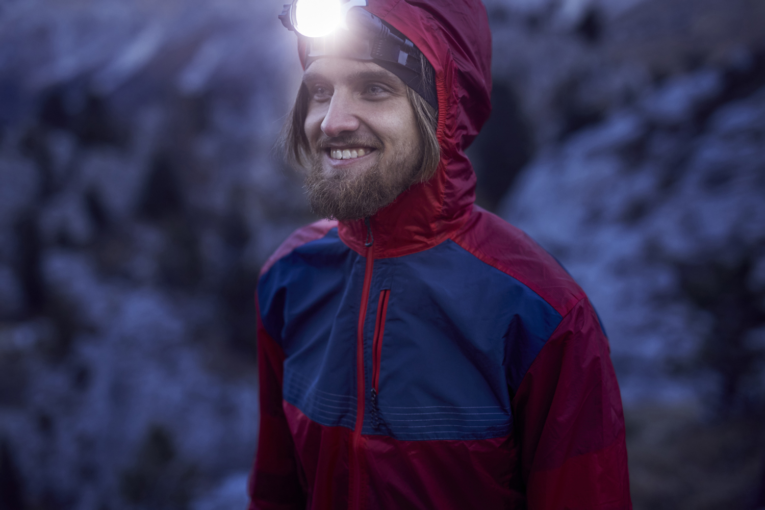 Young smiling man wearing a bright headlamp in the outdoors.