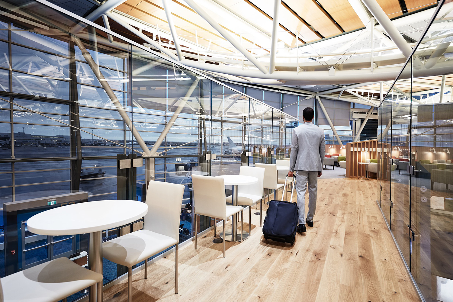 Man wheeling a rollaboard suitcase through a Priority Pass lounge in the Vancouver Airport.