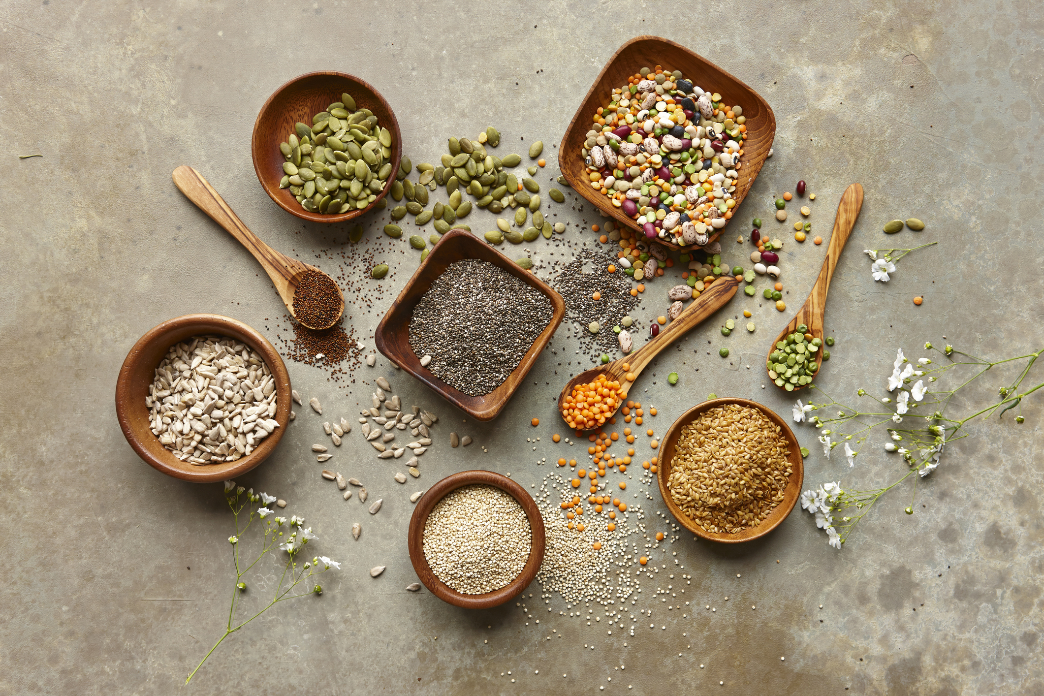 An assortment of edible seeds in bowls and spoons