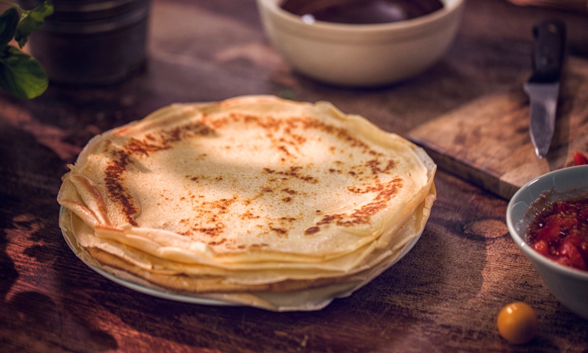 Preparing baked crepes pancakes with ham and tomatoes