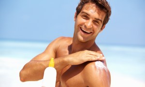 Portrait of attractive young man applying sunscreen lotion on body