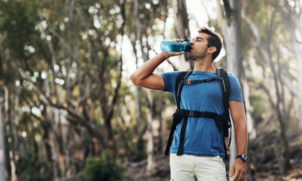 A carefree young man drinks water from a bottle while going for a hike up a mountain