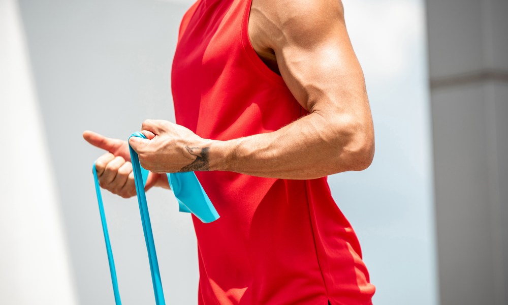 Fit muscular sports man doing bicep curl exercise with resistance band in the open air