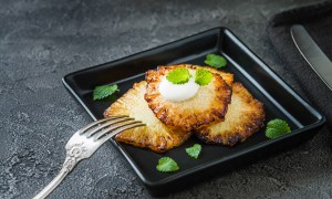 Fried pineapple slices with creme fraiche, mint in black square plate on dark background