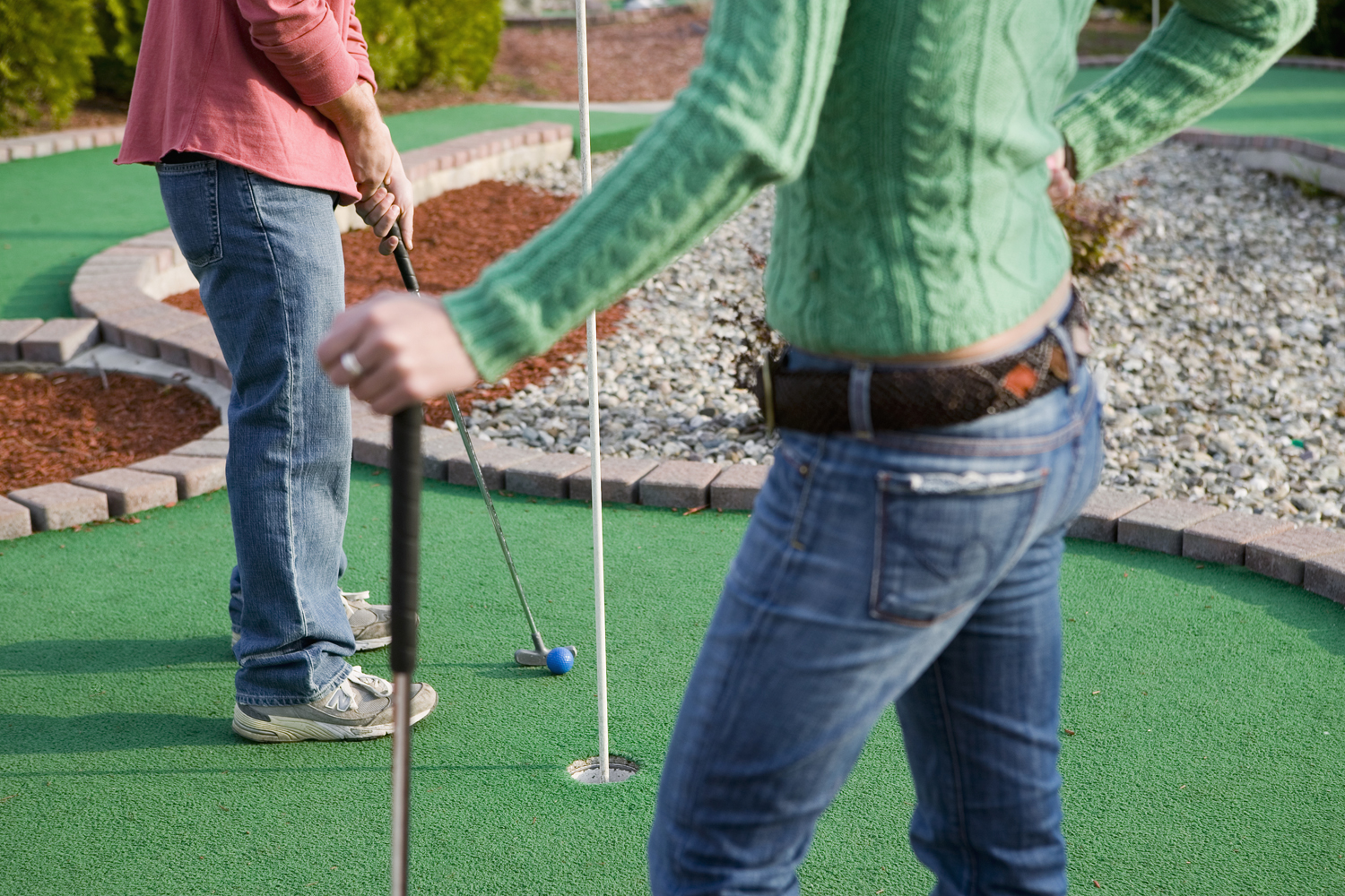 A lower body shot of a couple playing mini golf.