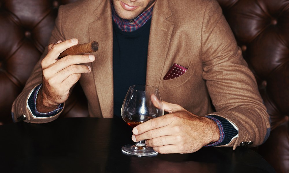 A stylish man drinking whiskey and smoking a cigar.