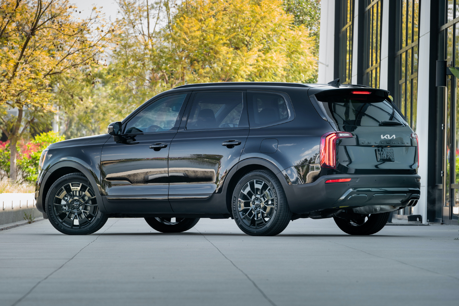 2022 Kia Telluride on a concrete path with yellow trees and a glass building in the back.