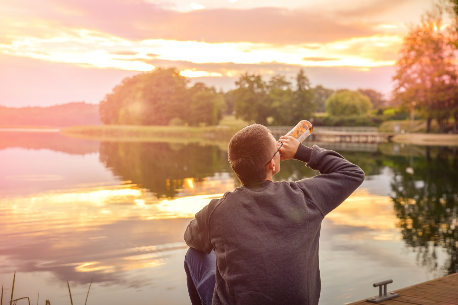 A man sitting and drinking beer on the pier at sunset.