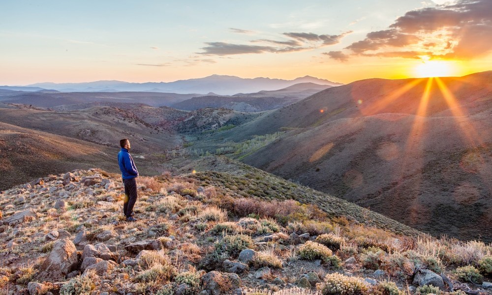 A person standing on a hill alone at sunset