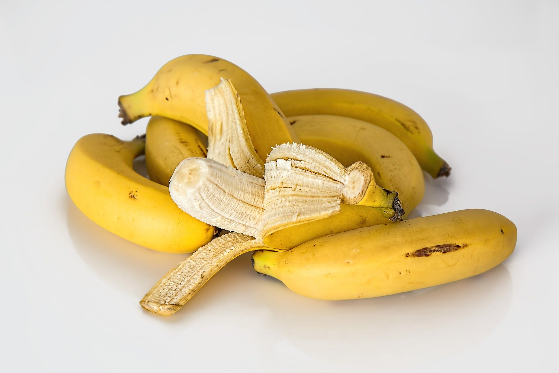 A bunch of bananas piled on top of each other with one of them peeled.