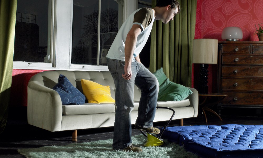 Young man using foot pump on air mattress in living room.