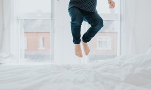 Cute little girl bouncing on a white bed in a bright room.