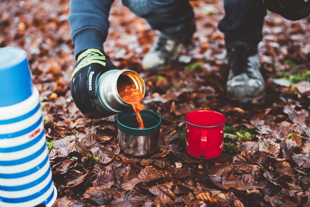 Person pouring coffee from a thermos on a hiking trail.