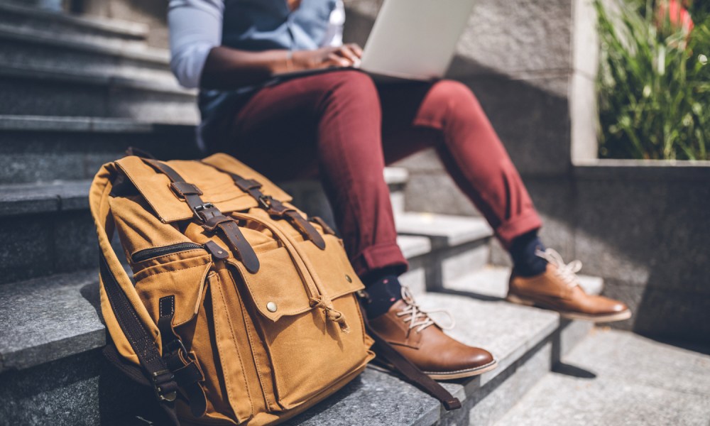 A man using a laptop beside a backpack by the stairs.