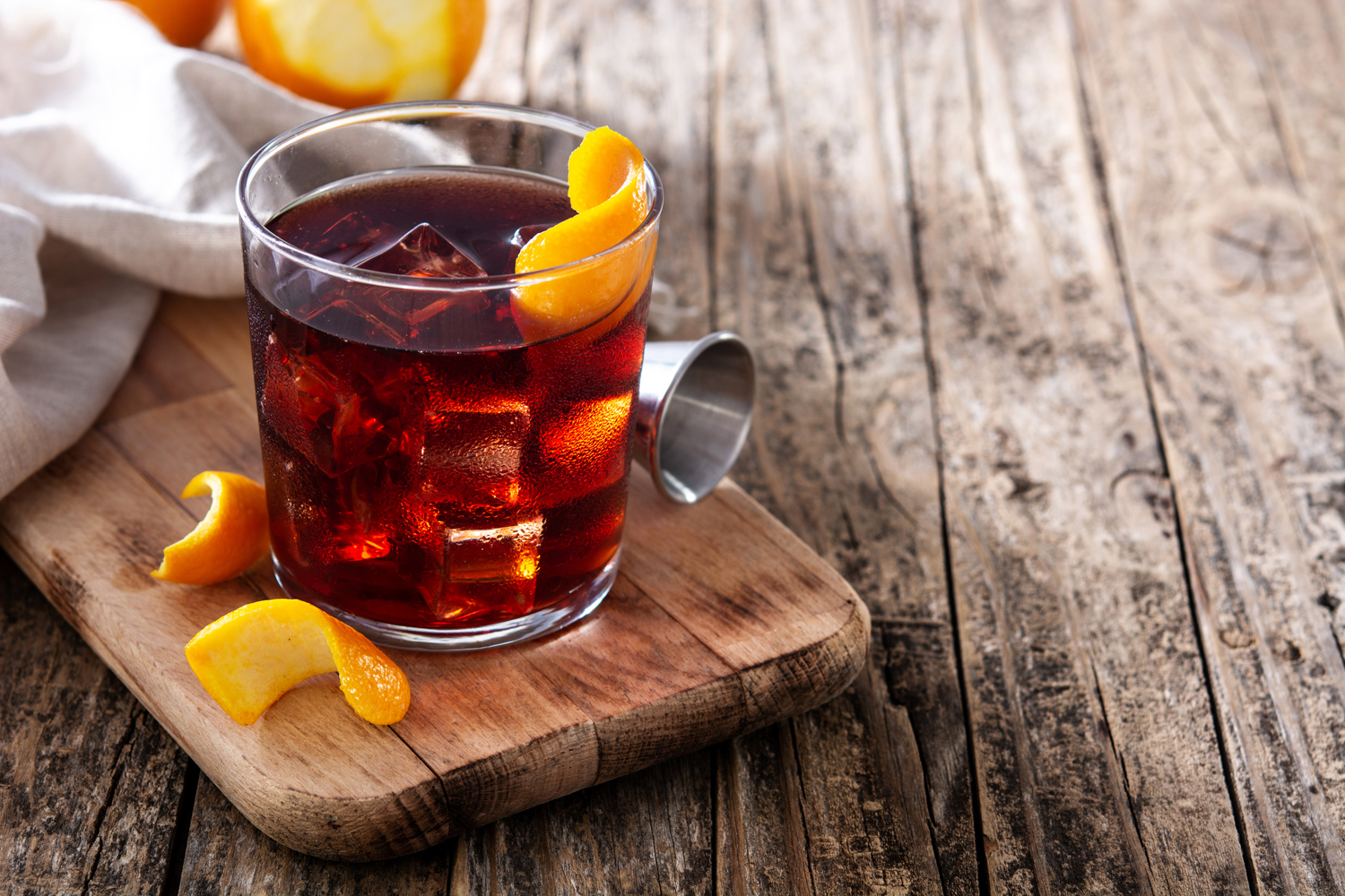 A Boulevardier cocktail with orange skin on a wooden table.