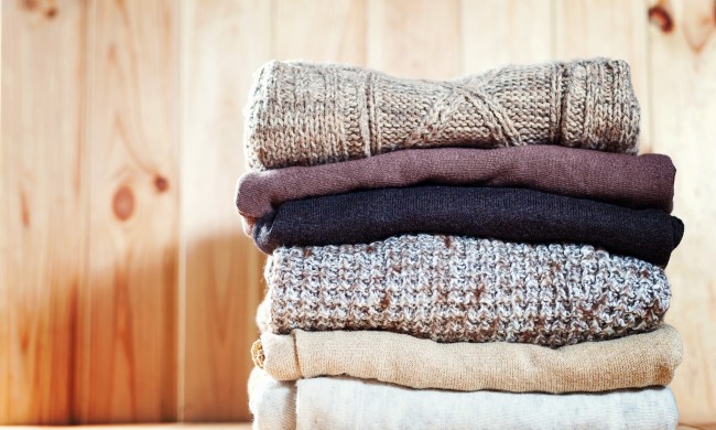 Knit cozy sweater folded in a pile on wooden background.