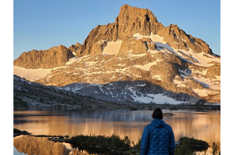 Man facing an alpine lake as the sunrises on a mountain peak, on the John Muir Trail Mountains image