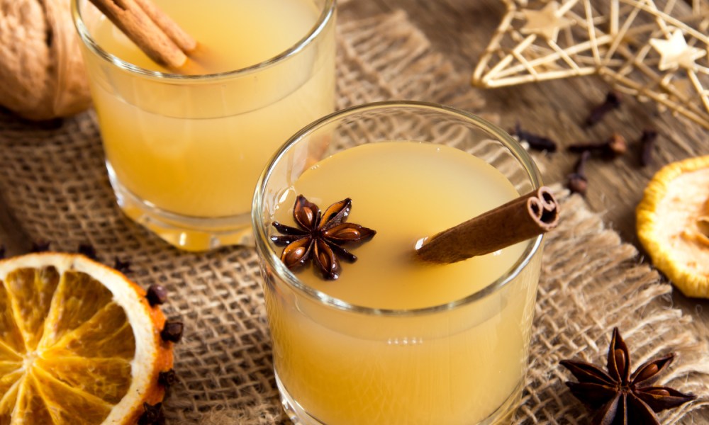 Two cups of hot toddies with cinnamon sticks on a piece of cloth.